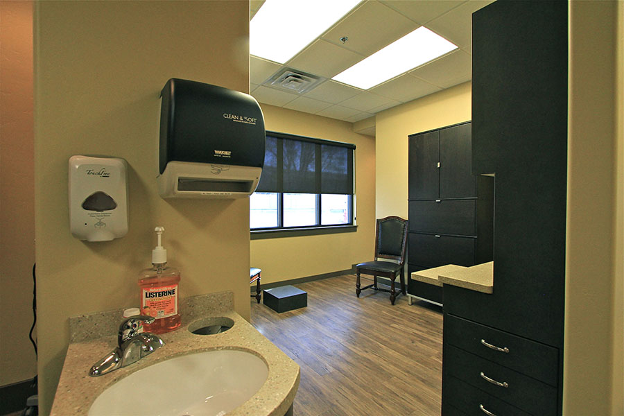 The image shows an interior view of a bathroom with a sink, mirror, and black paper towel dispenser.