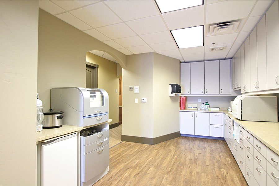 The image shows an interior view of a well-lit office space with a kitchenette area featuring appliances such as a microwave, refrigerator, and coffee maker.