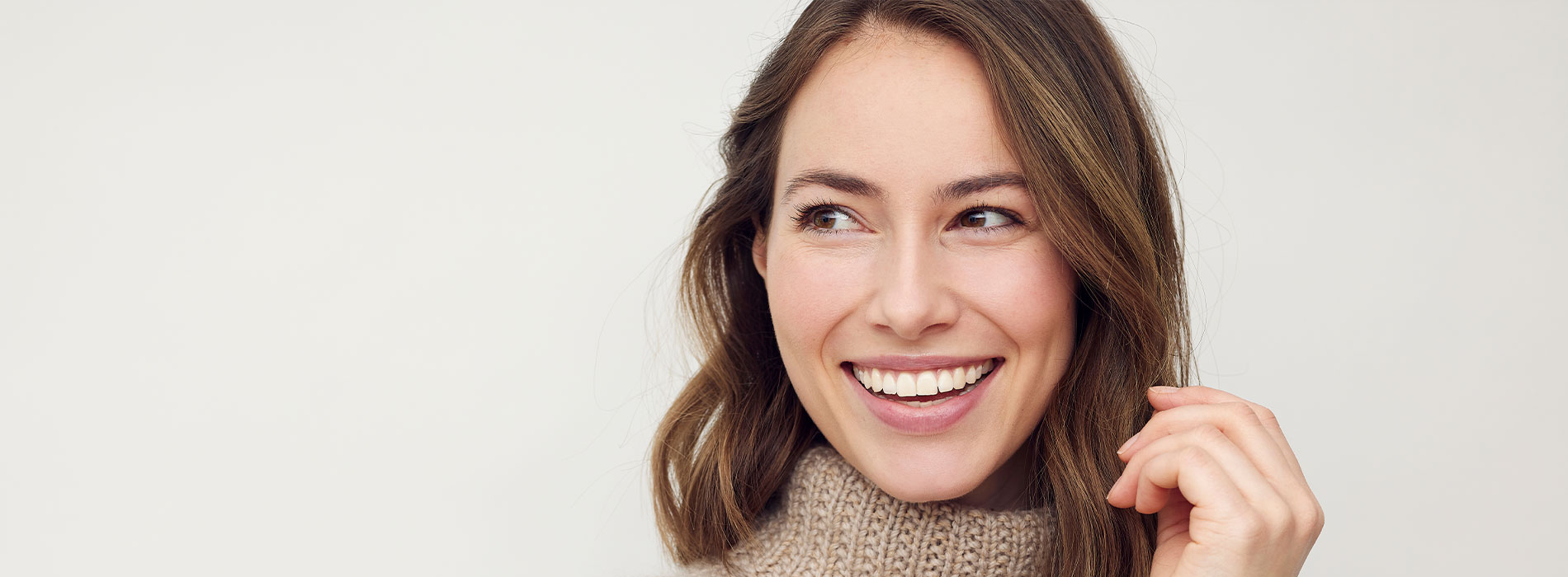 The image shows a woman with a smile, looking directly at the camera, against a light background.