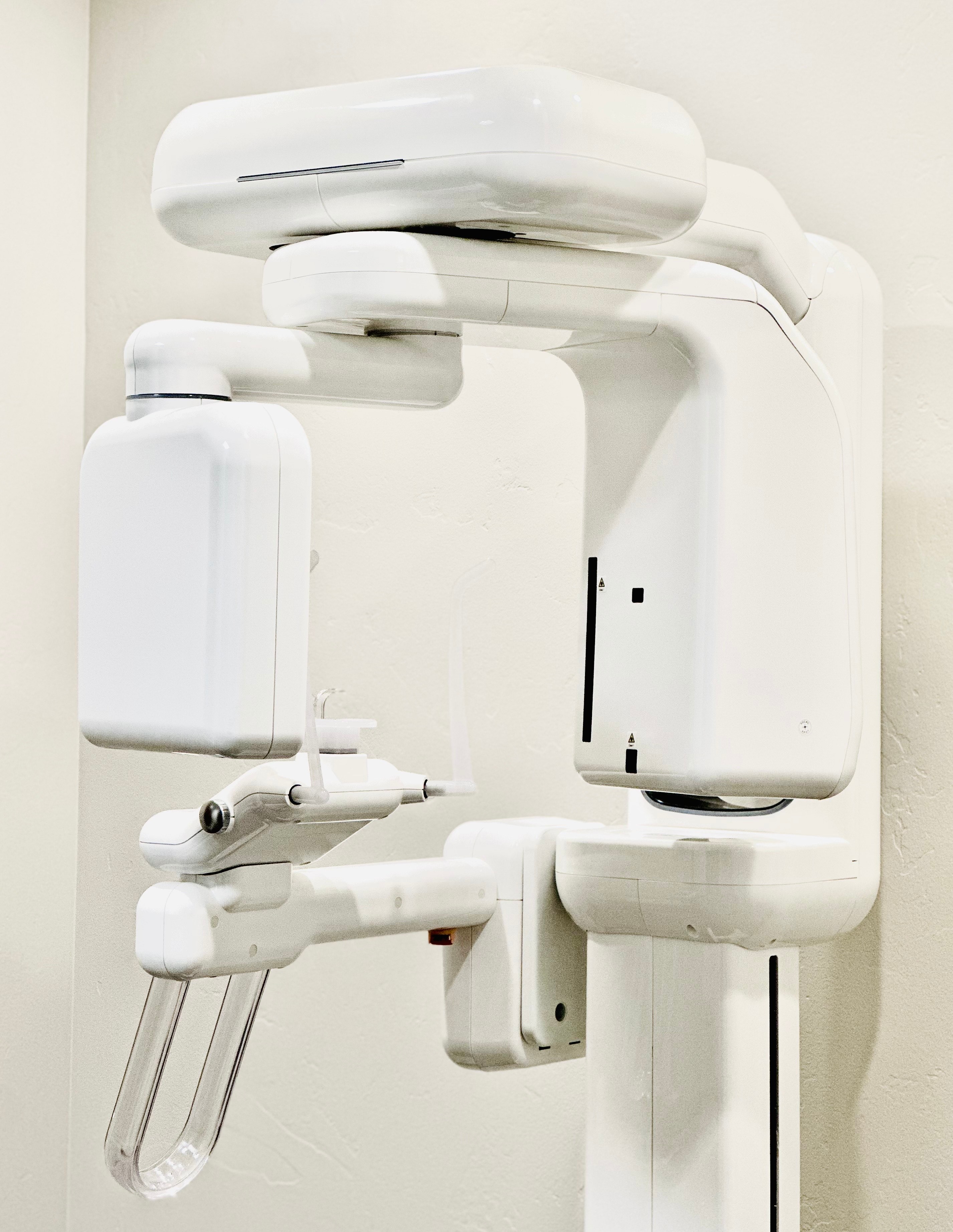 The image shows a modern dental chair with an overhead light and a digital display against a white wall.