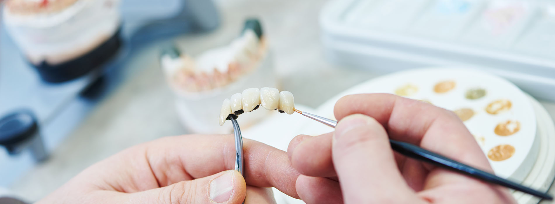 A person s hand holding a toothbrush over an open mouth model, with various dental tools and supplies in the background.