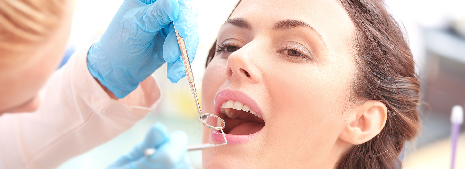 The image shows a woman receiving dental treatment from a dentist, with her mouth open and a dental instrument being used.