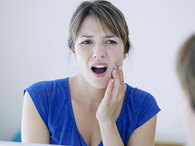 The image shows a woman with her mouth open, expressing surprise or shock, while holding her hand to her face, possibly indicating discomfort or pain.