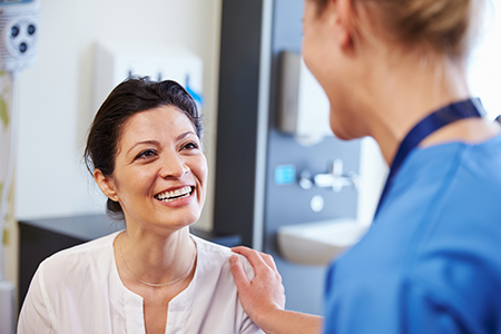 The image shows a woman in a white lab coat smiling at a man wearing a blue lanyard, with both individuals standing in a medical facility setting.
