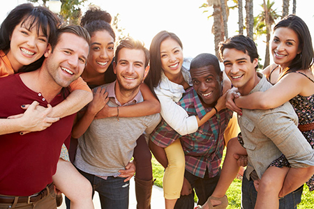 A group of young adults posing together for a photo with smiles on their faces, standing outdoors during daylight hours.