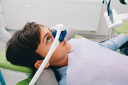 The image shows a person wearing an eye mask, lying on a dental chair with a dental mirror over their face, suggesting a dental examination or treatment is taking place.