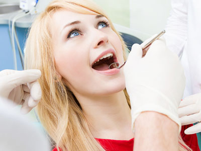 The image shows a dental professional performing a procedure on a patient s teeth while they are seated in a dental chair, with the patient wearing protective eyewear and a surgical mask.
