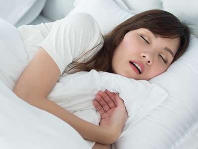 The image shows a woman lying in bed with her eyes closed, appearing to be asleep or resting.